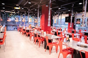 Interior de restaurante com cadeiras vermelhas, várias mesas e piso de azulejos.