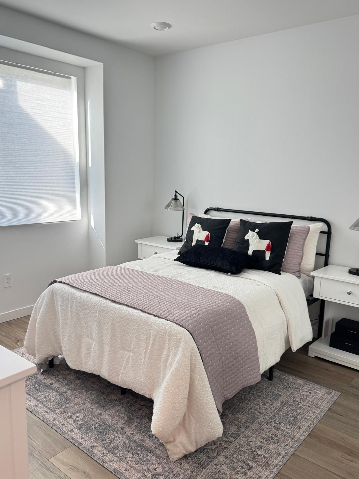 A bedroom with a bed, bedside tables, a lamp, a window, and a rug.