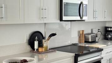 A modern kitchen with white cabinets, a stainless steel microwave, and a countertop with a bowl of fruit.