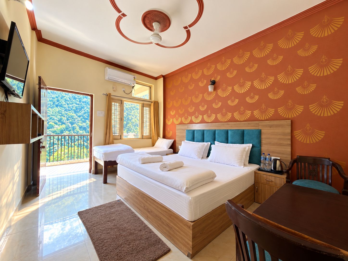 A hotel room with a large bed, a desk, a chair, a TV, and a balcony with a view of the forest.
