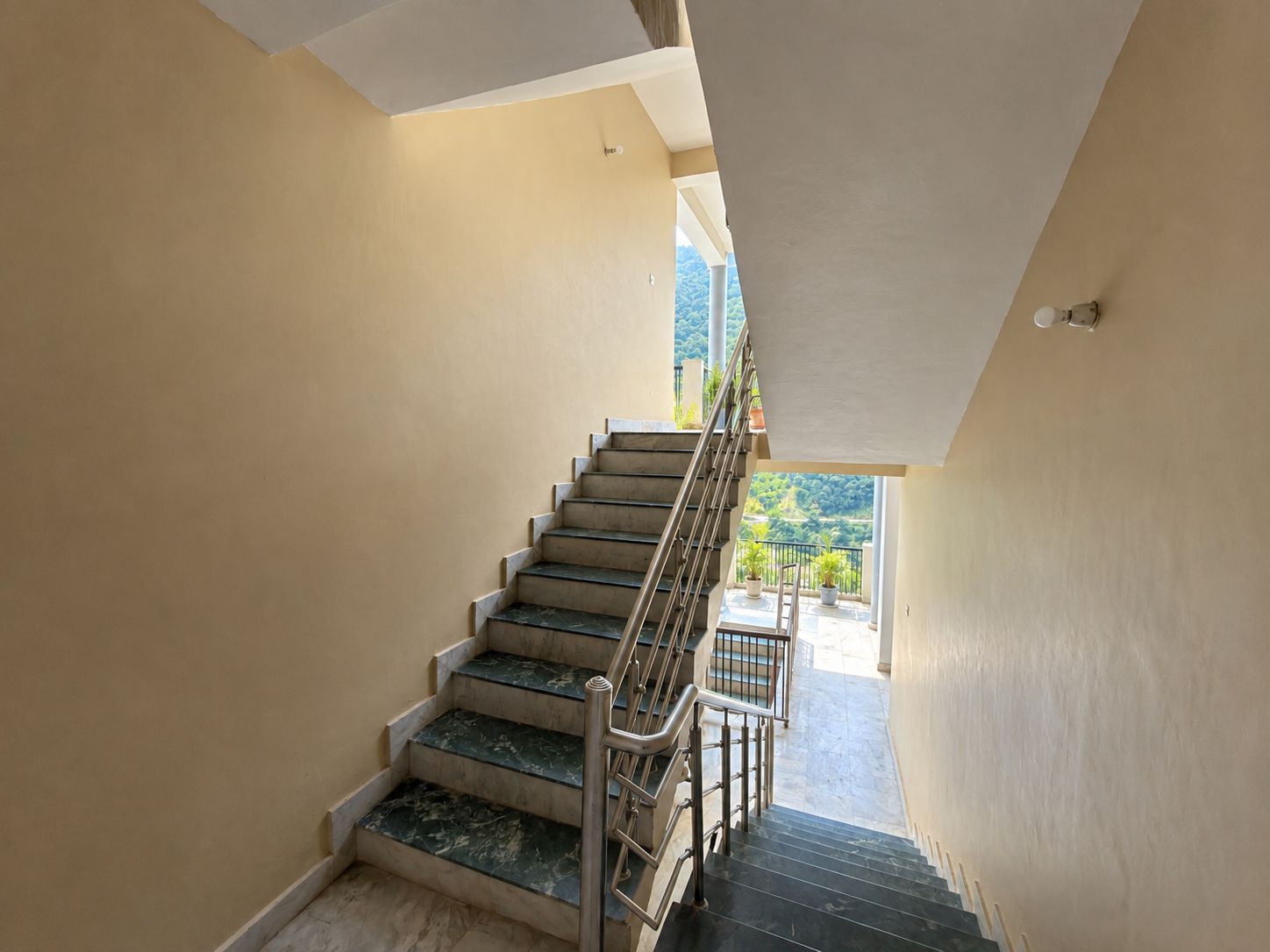 A staircase with a metal railing leading to a balcony with potted plants.