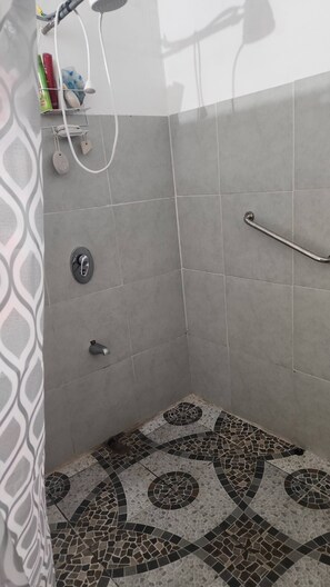 A shower area with tiled walls, a showerhead, a handrail, and a patterned floor.