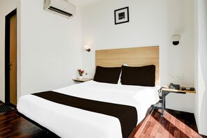 Een hotelkamer met een bed, nachtkastje, lamp en een aan de muur bevestigde airconditioner.