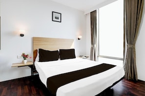 Een hotelkamer met een groot bed, een nachtkastje met een lamp, een schilderij aan de muur en een raam met gordijnen.