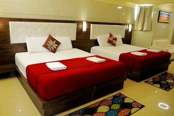 Une chambre d’hôtel avec deux lits, chacun recouvert d’une couverture rouge et agrémenté d’oreillers blancs, avec une tête de lit en bois et un tapis à motifs.