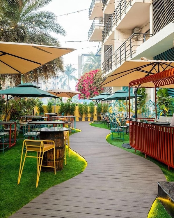 Un espacio patio al aire libre con mesas, sillas, un pasillo de madera y una zona de bar.