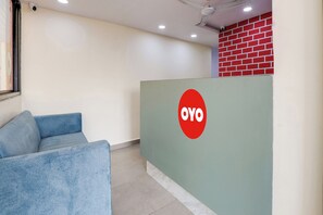 Una zona de recepción con un sofá azul, un mostrador verde con un logotipo rojo y una pared de ladrillo rojo.