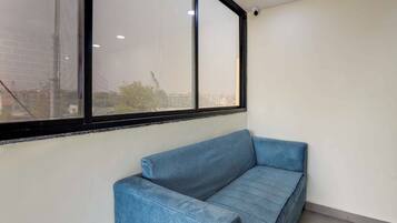 A corner room with a blue sofa, a large window with a black frame, and a white wall.