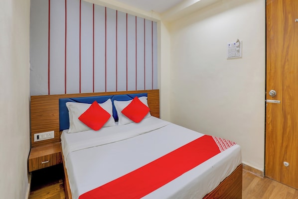 Una habitación de hotel con cama, cabecera de madera, pared a rayas rojas y blancas, y una puerta de madera.