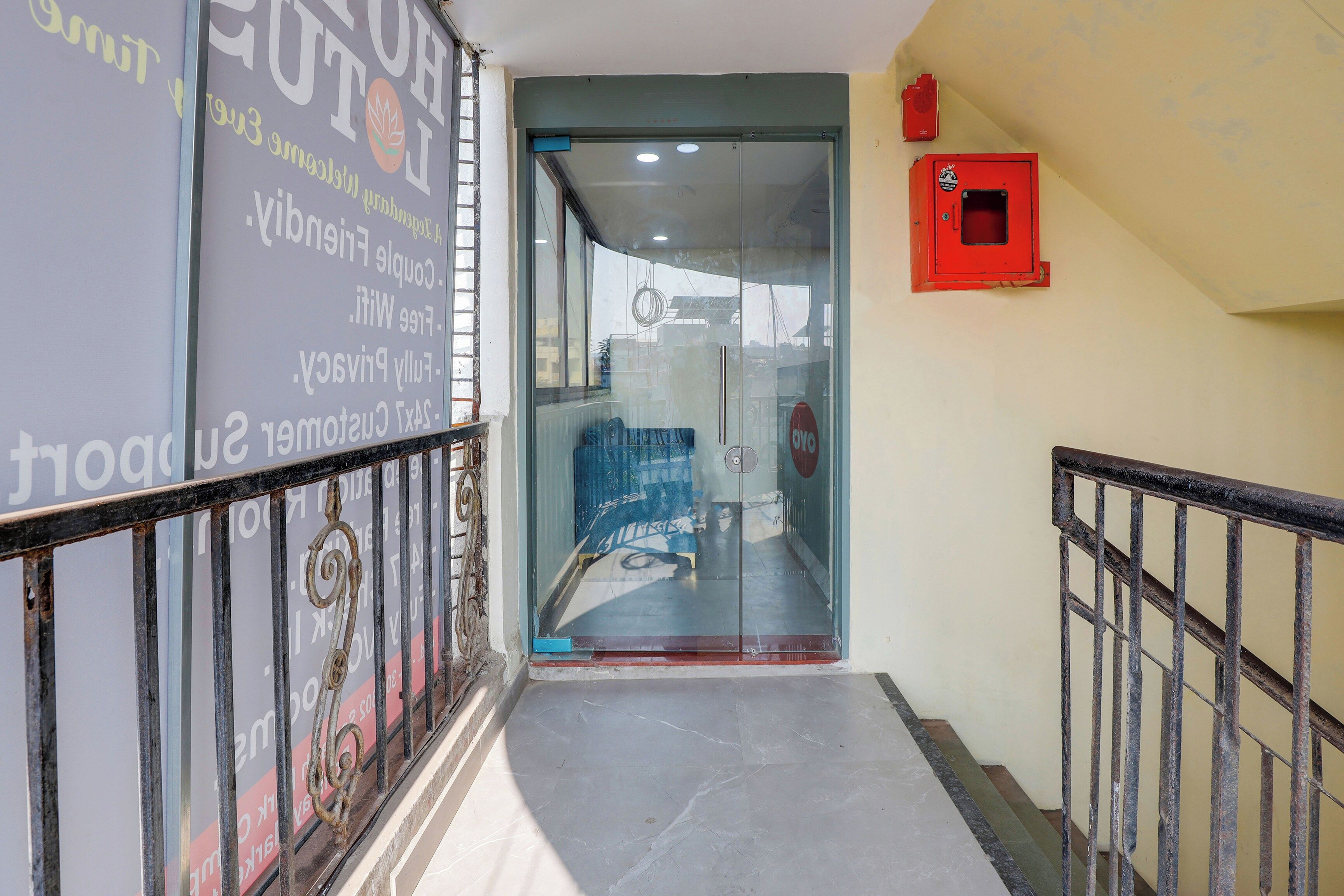 A hallway with a glass door entrance, a red fire alarm box on the wall, and a metal railing.