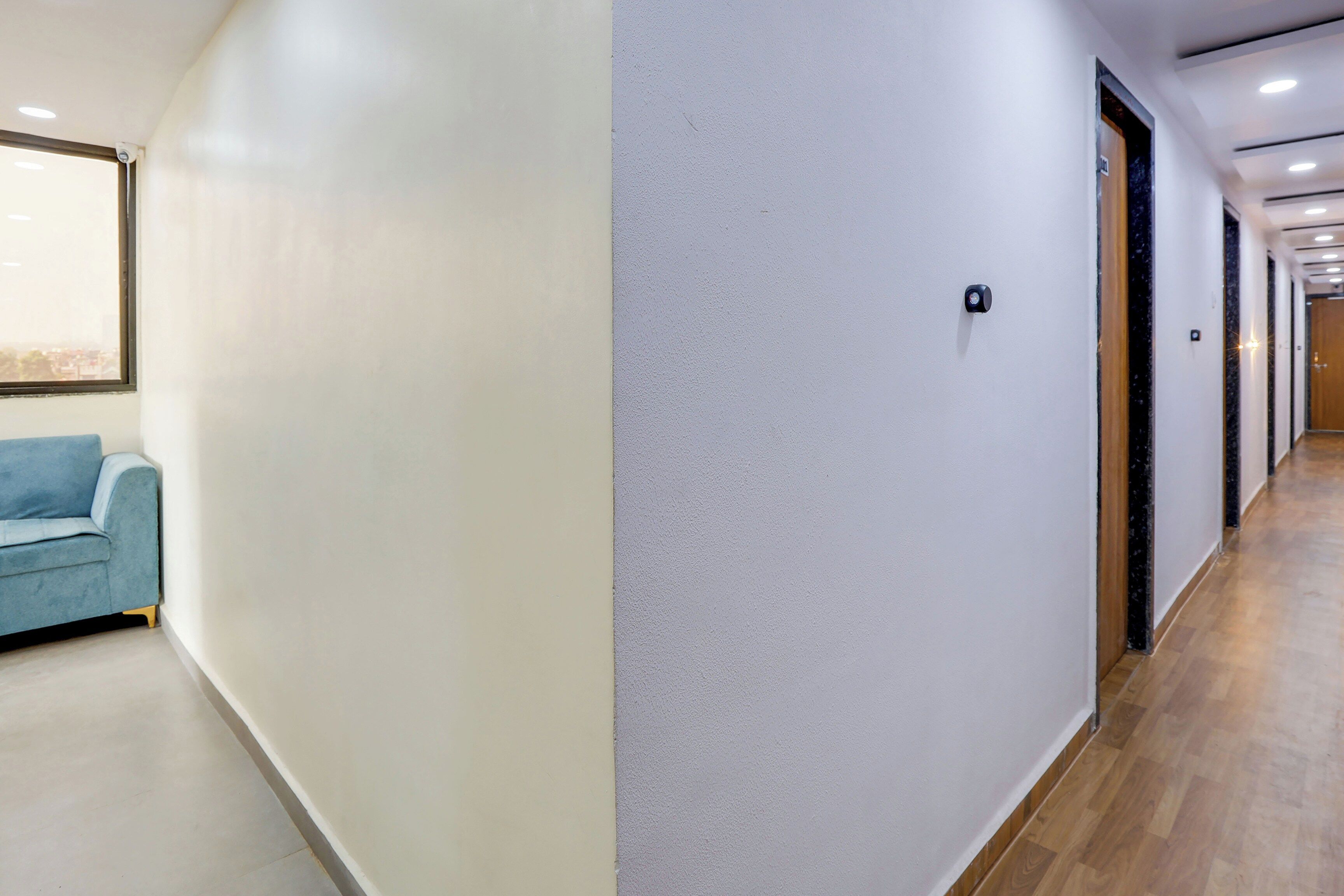 Un pasillo con un sofá azul, una pared texturizada y una puerta con cámara de seguridad.