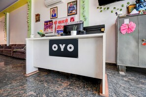 Een receptiebalie met een bordje waarop 'OYO' staat, in een hotellobby met een bank en een kast.