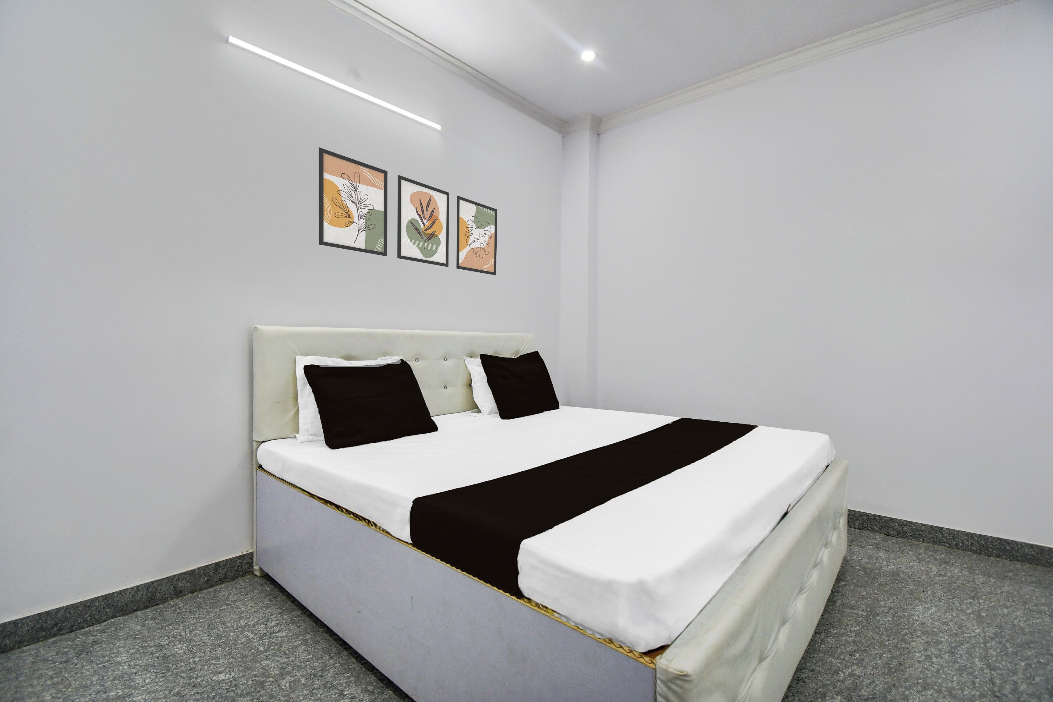 A hotel room with a bed, a headboard, a wall-mounted light fixture, and three framed pictures.