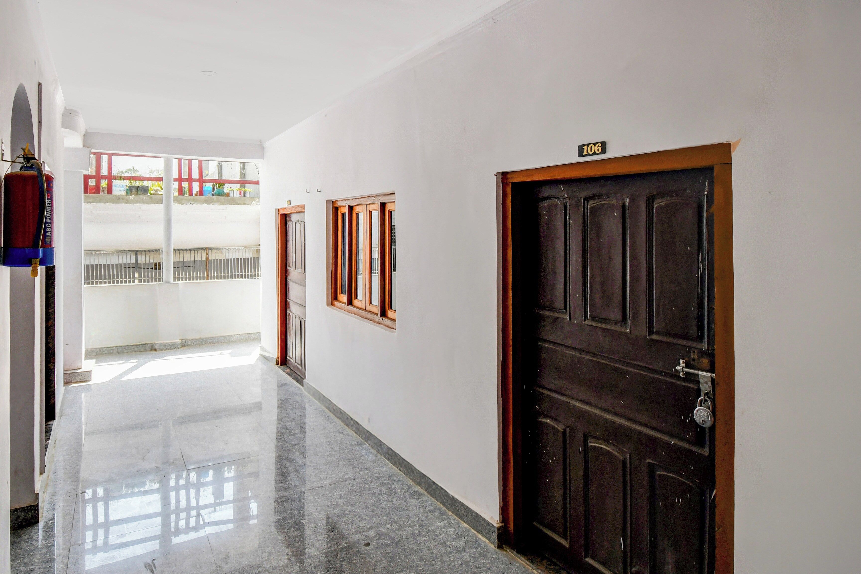 A corridor with a fire extinguisher, a door marked '106', and a window with a view of a balcony.