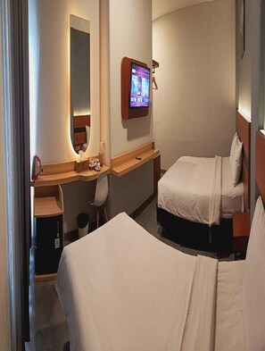 Una habitación de hotel con una cama, un escritorio con silla, un televisor y un espejo.