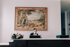 Vastaanottotiski, jonka yläpuolella on suuri kehystetty taulu, jossa on kuvattuna puutarhamaisema.