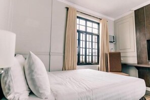 Hotellihuone, jossa on sänky, työpöytä, tuoli, ikkuna verhoilla ja seinälle asennettu ilmastointilaite.