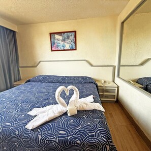 Una habitación de hotel con una cama, una mesita de noche con un teléfono, un cuadro en la pared y un espejo.
