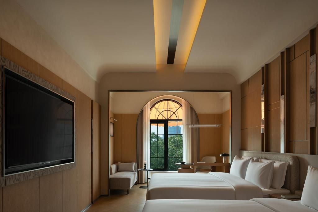 A hotel room with a large bed, a TV, and a view of the outdoors through a window.