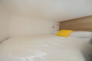 A single bed with a wooden headboard, a white comforter, and a yellow pillow. - Warsaw | Staszica 4 | Bright Studio | Mezzanine (Warszawa)
