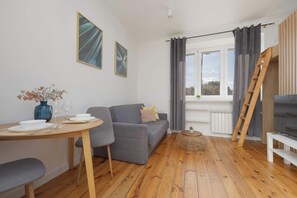 Een moderne woonkamer met een bank, een eettafel met stoelen, een televisie en een raam met gordijnen.