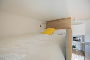 Een slaapkamer met een bed, een nachtkastje, een magnetron en een kleine plant.