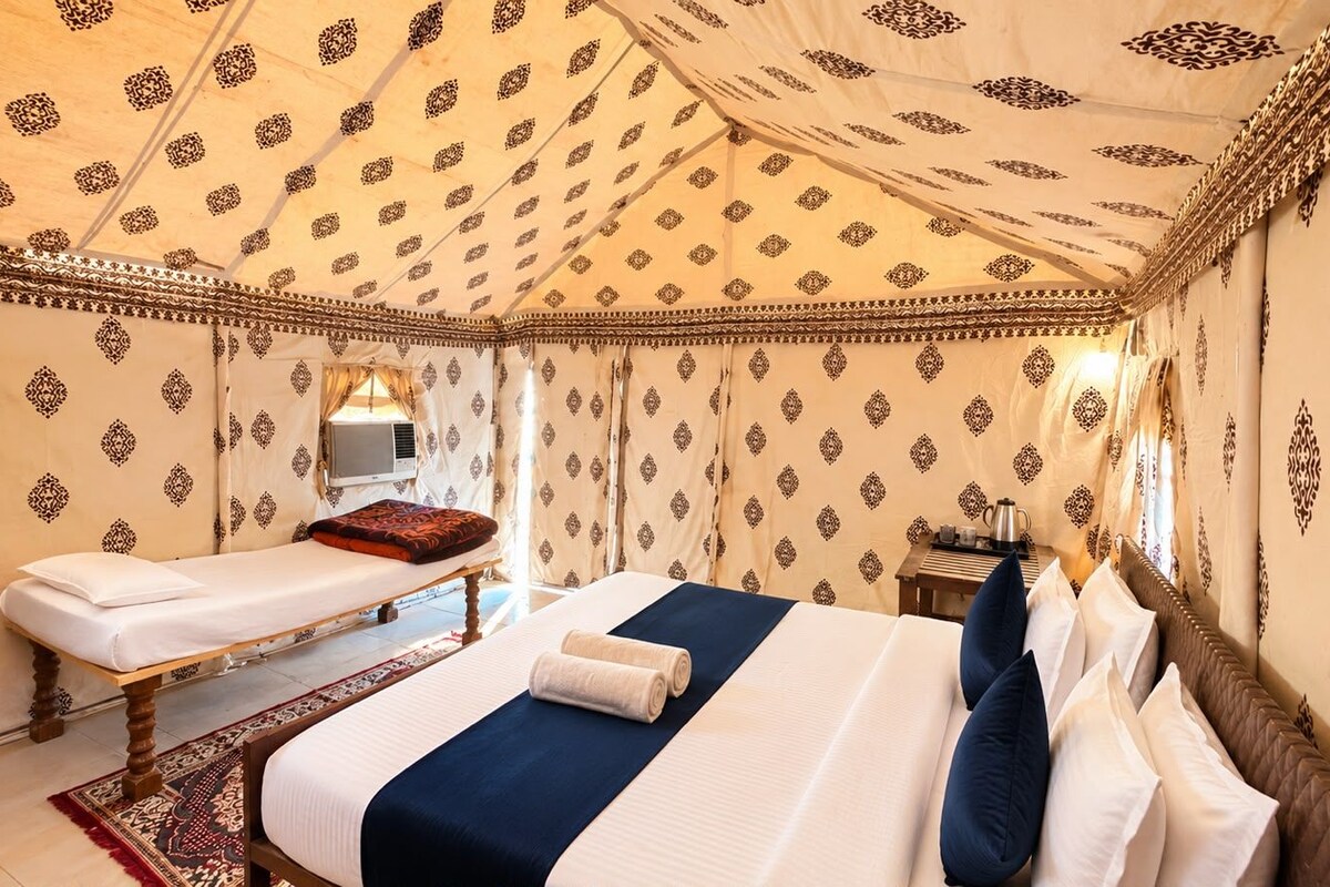 A room with two beds, a small table with a kettle, and patterned walls.