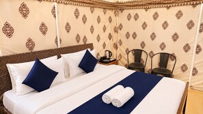 Habitación de hotel con cama, almohadas, mesita de noche, una silla y cortina con diseño estampado.