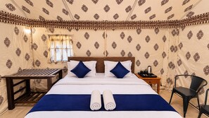 Habitación de hotel con cama, almohadas, mesita de noche, una silla y ventana con cortinas.