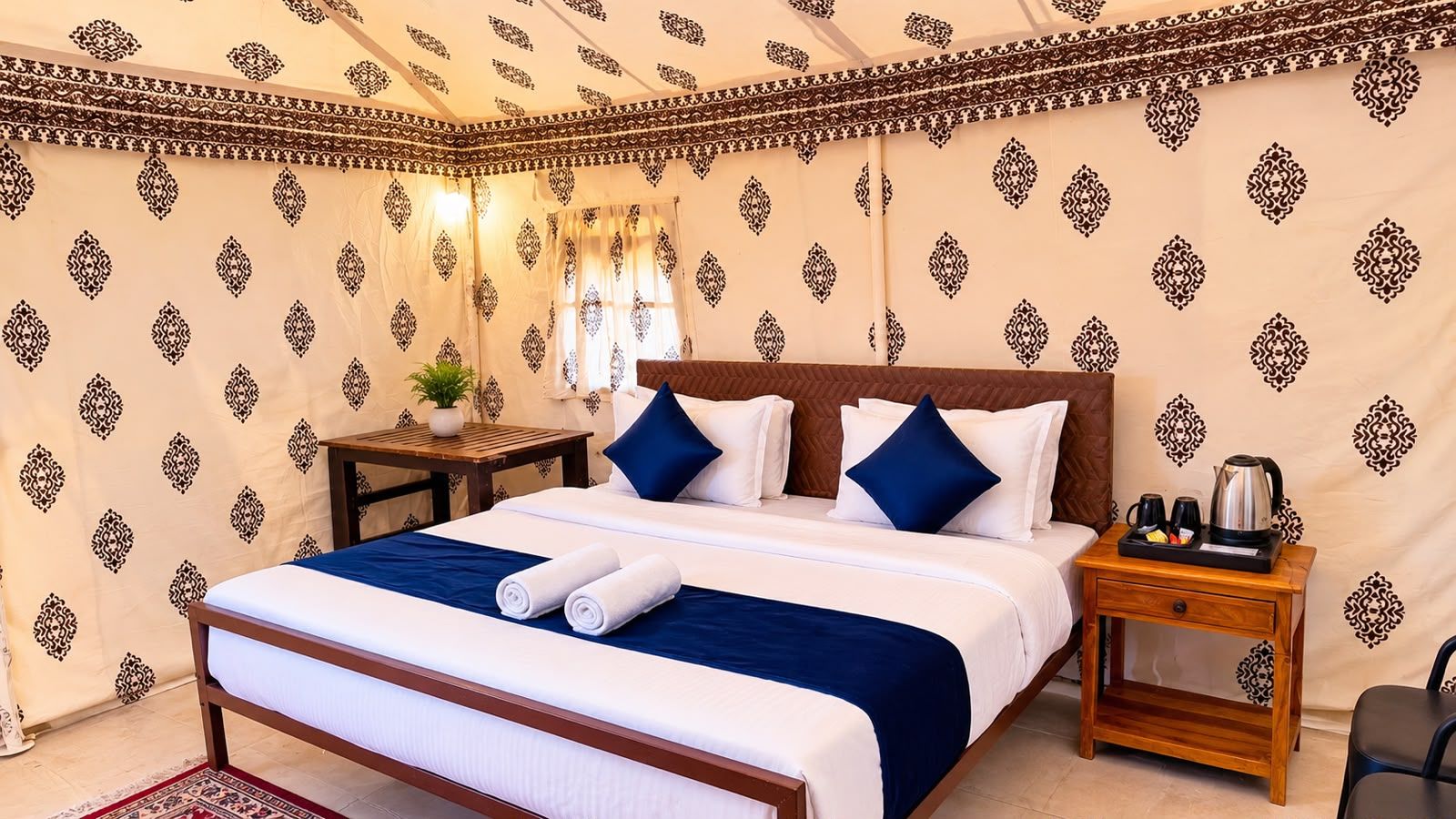 Habitación de hotel con cama, almohadas, mesita de noche, una mesa con planta y cafetera.