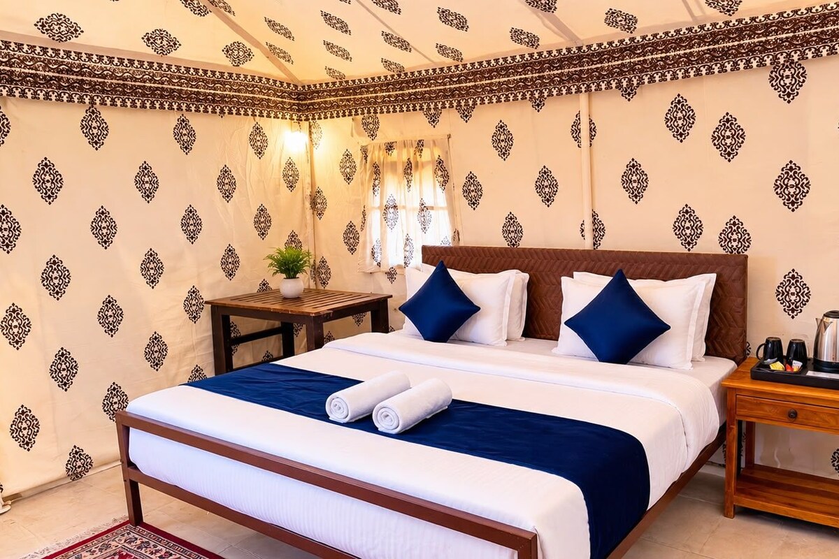 Habitación de hotel con cama, almohadas, mesita de noche, una mesa con planta y cafetera.