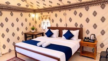 Habitación de hotel con cama, almohadas, mesita de noche, una mesa con planta y cafetera.