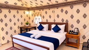 Habitación de hotel con cama, almohadas, mesita de noche, una mesa con planta y cafetera.
