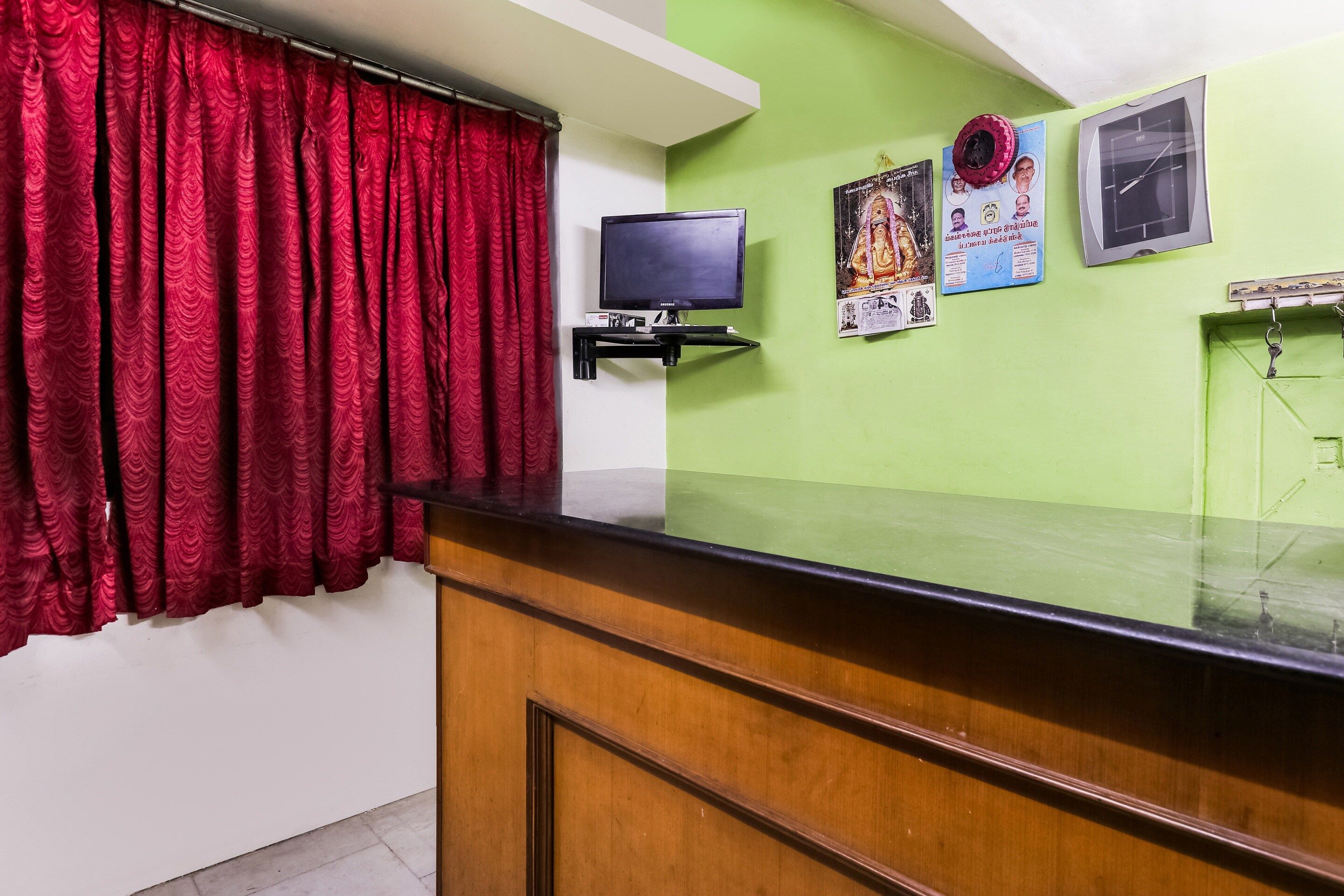 Un área de recepción con mostrador de madera, televisor montado en la pared y una cortina roja.