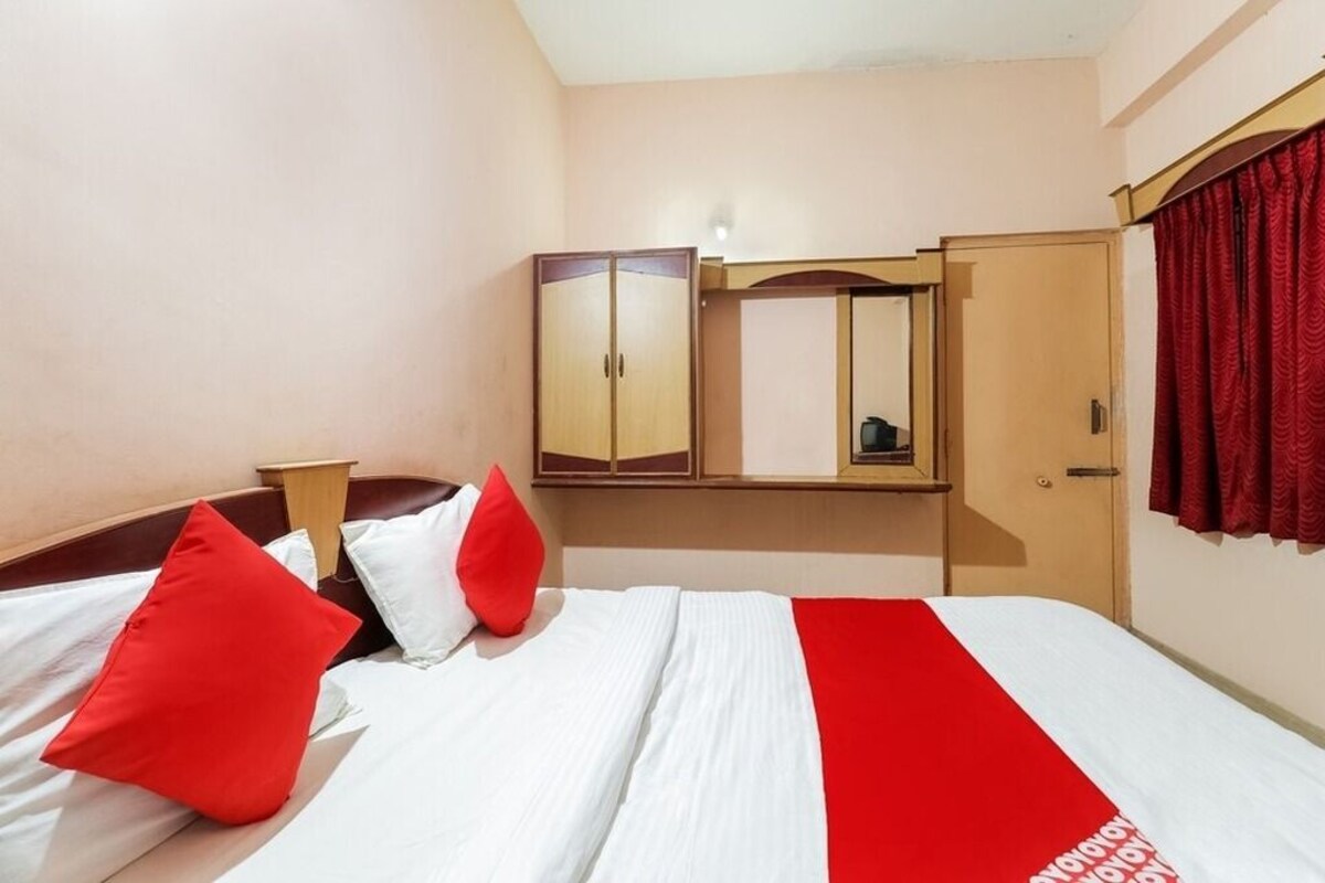Una habitación de hotel con cama, armario, espejo y cortina roja.