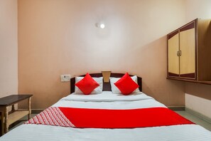 Una cama individual con colcha roja y blanca, dos almohadas rojas, cabecera de madera, una mesita de noche y un armario.