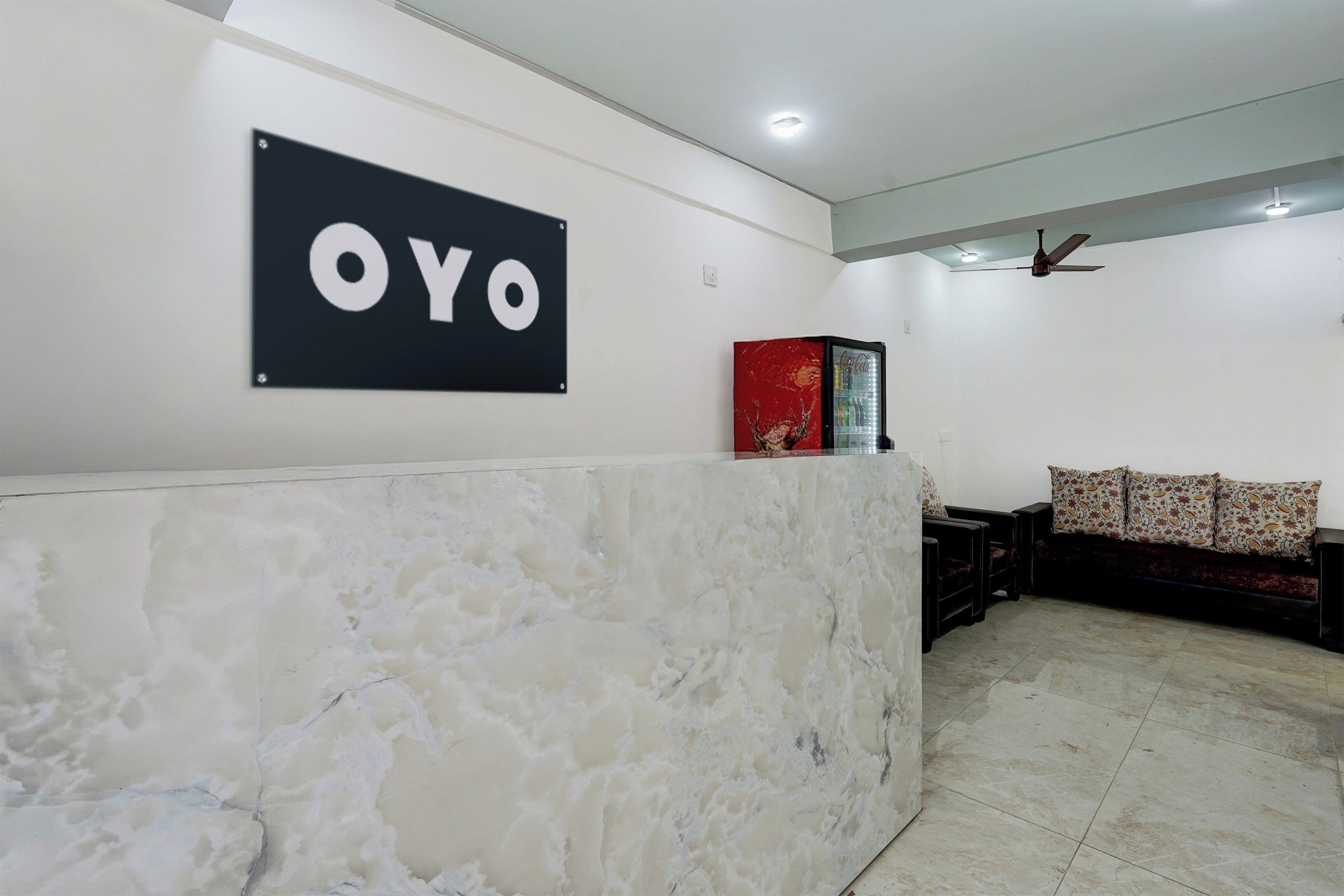A reception area with a marble counter, a wall-mounted sign reading 'OYO', a ceiling fan, and a sofa with patterned cushions.