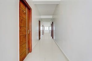 Un largo y estrecho pasillo con puertas de madera a un lado y paredes blancas al otro.
