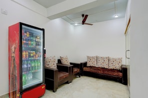 Una sala de estar con un refrigerador rojo lleno de bebidas, un ventilador de techo y un sofá con cojines estampados.