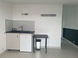 Een kleine keuken met een spoelbak, een koelkastje en een prullenbak.
