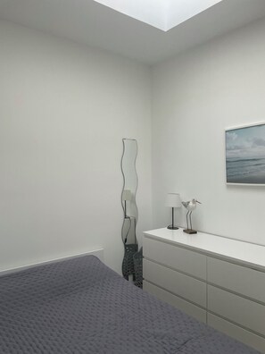 Ein modernes Schlafzimmer mit einem Bett, einer Kommode, einer Wandleuchte und einem Gemälde.