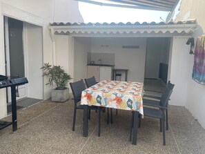 Eine Terrasse mit Tisch, Stühlen, einem Blumentopf und einem Grill.