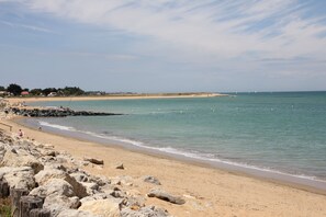 Ein Strand mit felsigem Ufer, ruhiger See und Gebäuden in der Ferne.