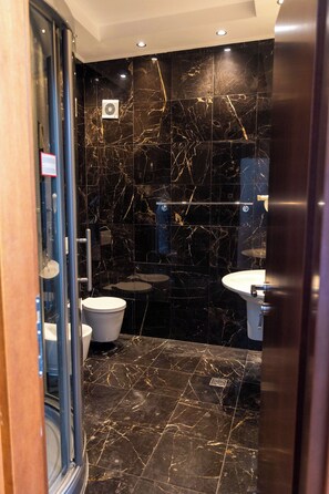 Un baño con piso de mármol negro, dos lavamanos y un inodoro.