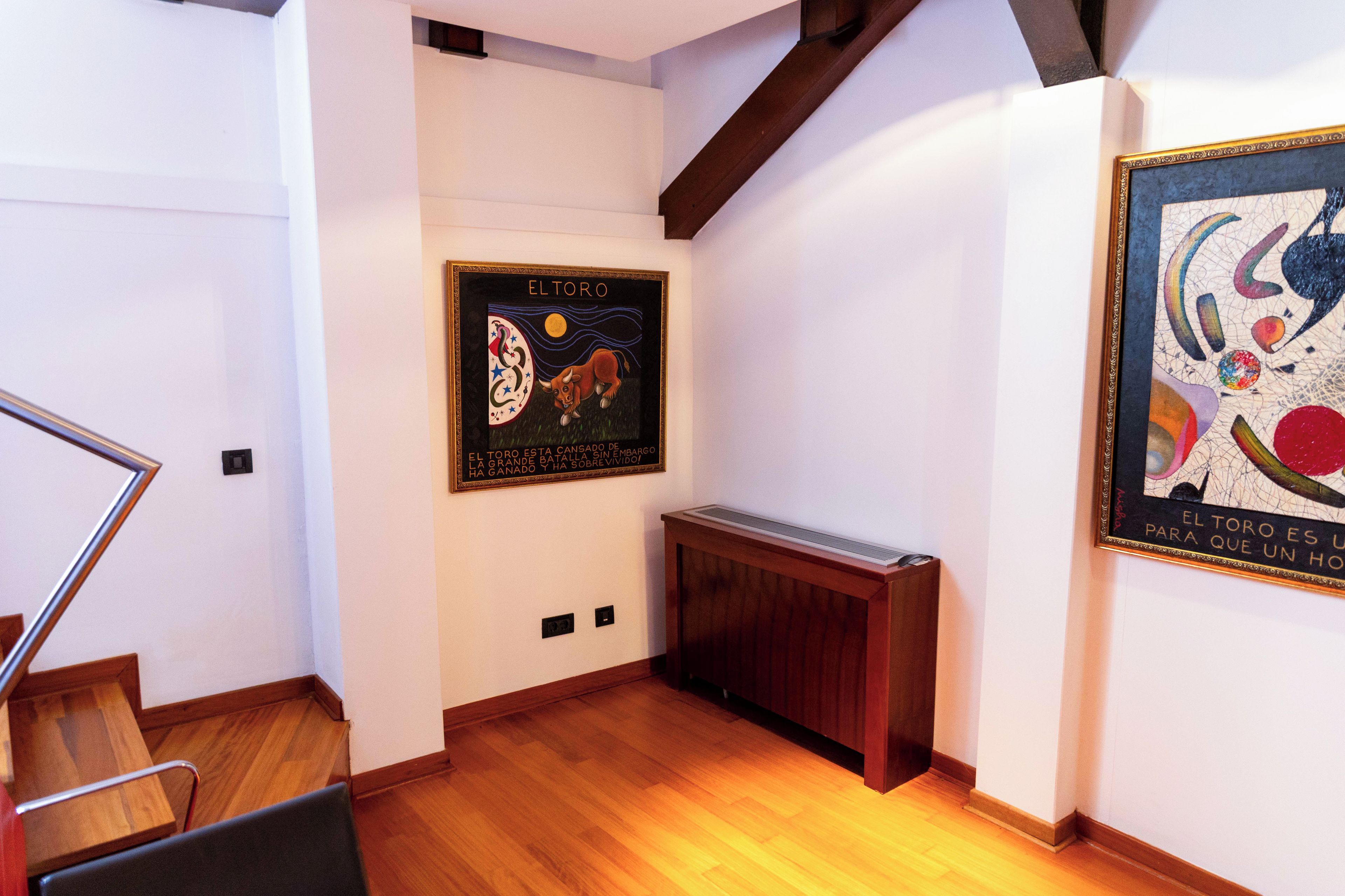 A hallway with wooden flooring, a radiator, and two framed artworks on the walls.