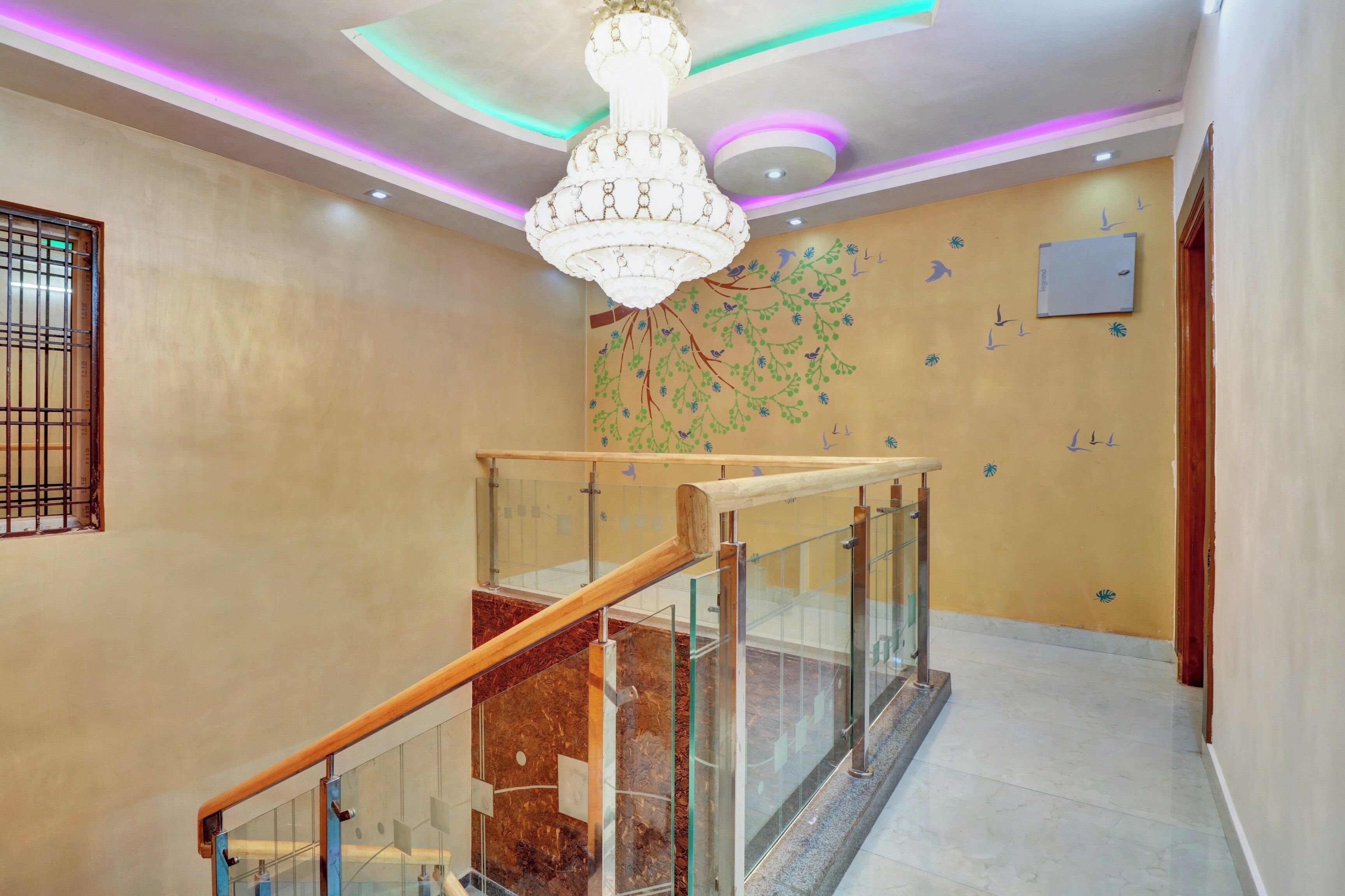 A modern interior with a glass railing staircase, a decorative wall mural, and a chandelier.