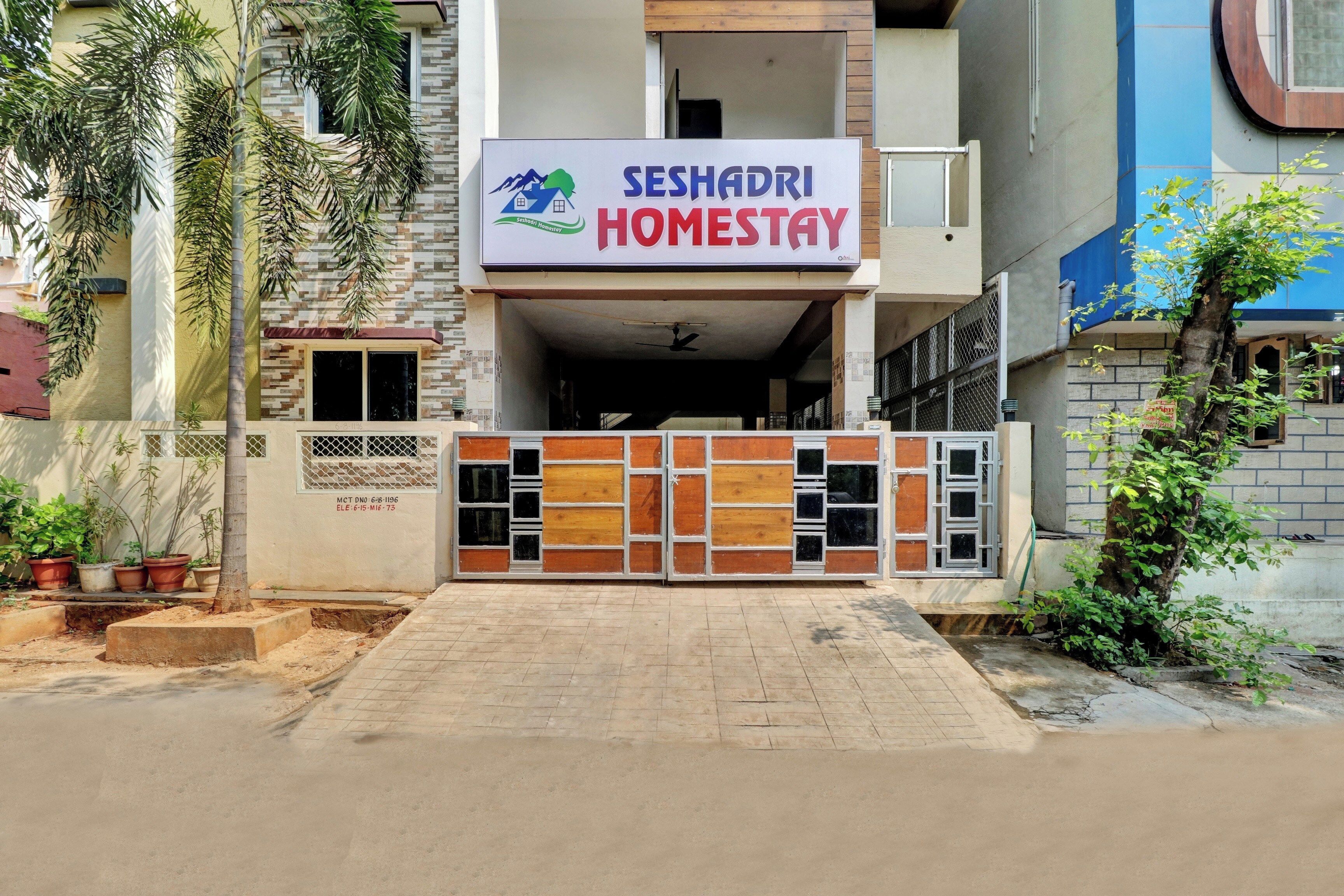 A building with a sign for 'SESHADRI HOMESTAY' featuring a logo with a house and mountains.