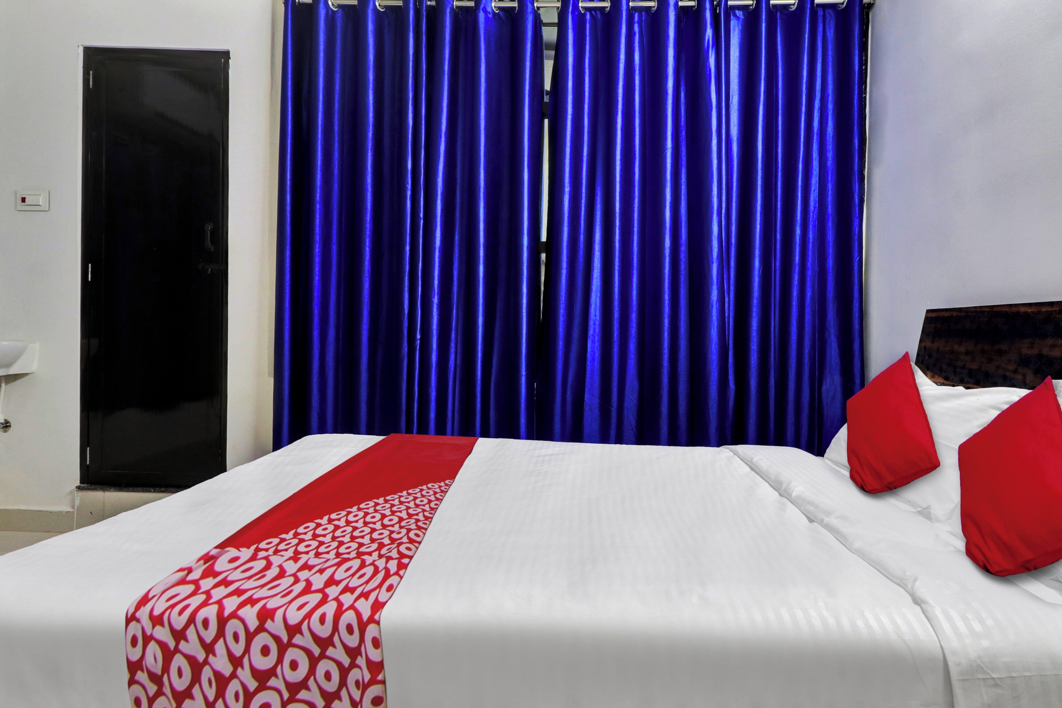 A hotel room with a bed, red and white bedding, a blue curtain, and a closed door.