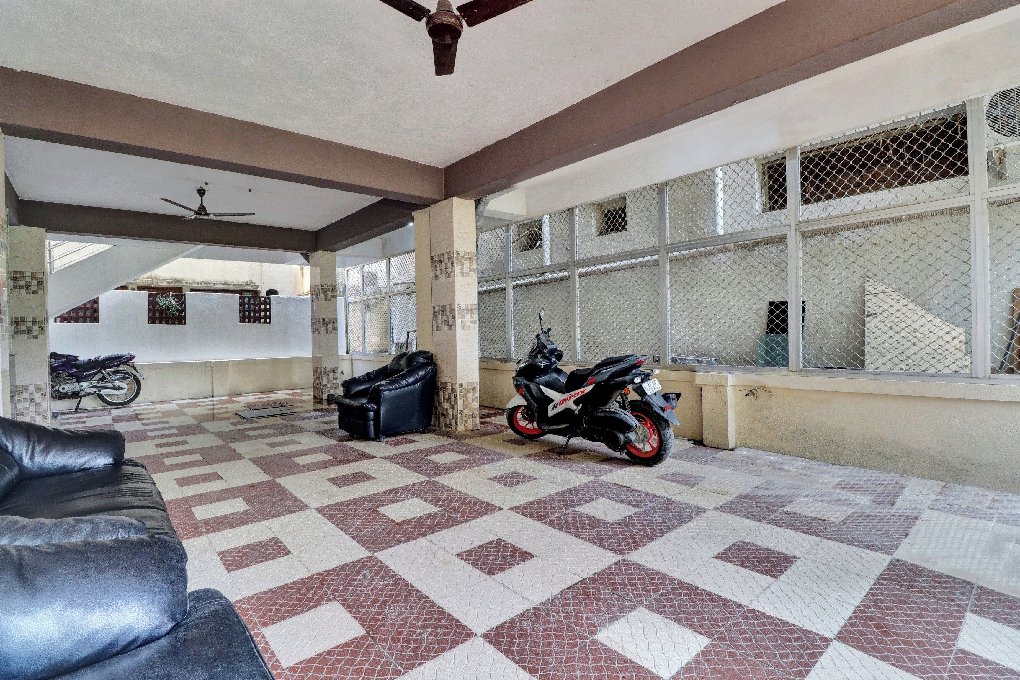 Un espace extérieur abrité, doté d’un sol à motifs, d’un ventilateur de plafond et d’une moto garée près d’un mur.