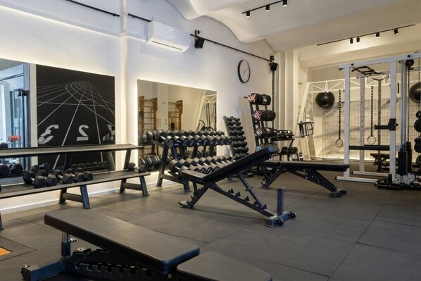 Ein Fitnessstudio mit verschiedenen Trainingsgeräten, darunter Kurzhanteln, Bänke und Kraftgeräte.